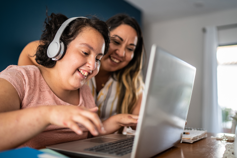 Girl with intellectual and developmental disabilities using a computer with a headset with her mother watching.