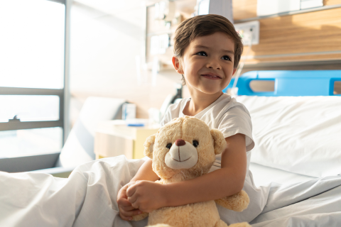 Young boy in a hospital bed holding a teddy bear.
